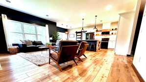 A modern living room with a dining area, wooden flooring, and a kitchen in the background. - Jay Cooke Park and Spirit Mtn Retreat with wood-burning sauna and game room  (Esko)