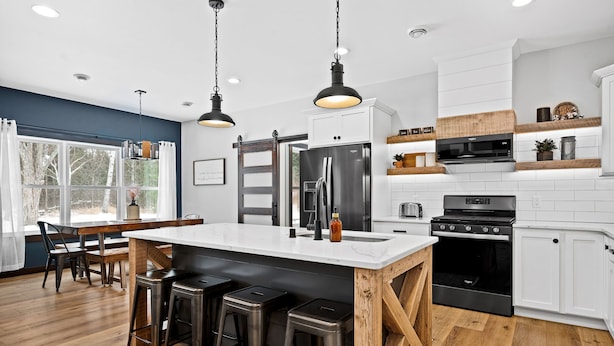 A modern kitchen with a large island, stainless steel appliances, and a wooden accent wall. - Jay Cooke Park and Spirit Mtn Retreat with wood-burning sauna and game room  (Esko)