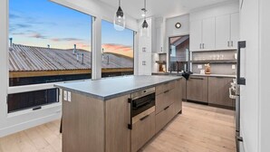A modern kitchen with a large island, wooden cabinets, and a view of a rooftop.