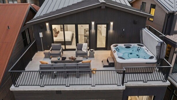 A modern rooftop terrace with a hot tub, outdoor seating, and a view of the cityscape.