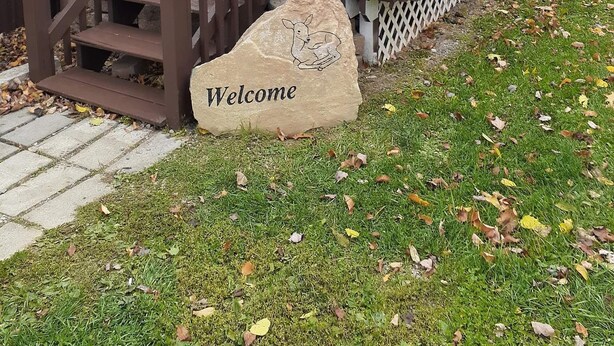 A cabin with a wooden deck, a stone with 'Welcome' engraved, and a mailbox.