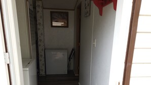 A narrow hallway with a wooden floor, a brown doormat, a white radiator, and a red shelf on the right wall.