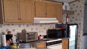 A compact kitchen with wooden cabinets, a built-in stove, a microwave, and a refrigerator.