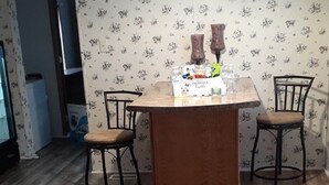 A dining area with a wooden table, two chairs, a hanging light fixture, and a floral wallpaper.