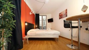 A modern bedroom with a bed, a small table, a plant, a TV, and a window with a view. - 101 - Studio confortable avec kitchenette Paris 5 (Paris)