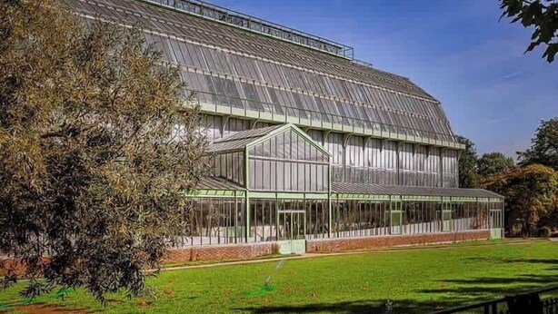 A large greenhouse with a glass roof and walls, surrounded by a grassy area and a black fence. - 101 - Studio confortable avec kitchenette Paris 5 (Paris)