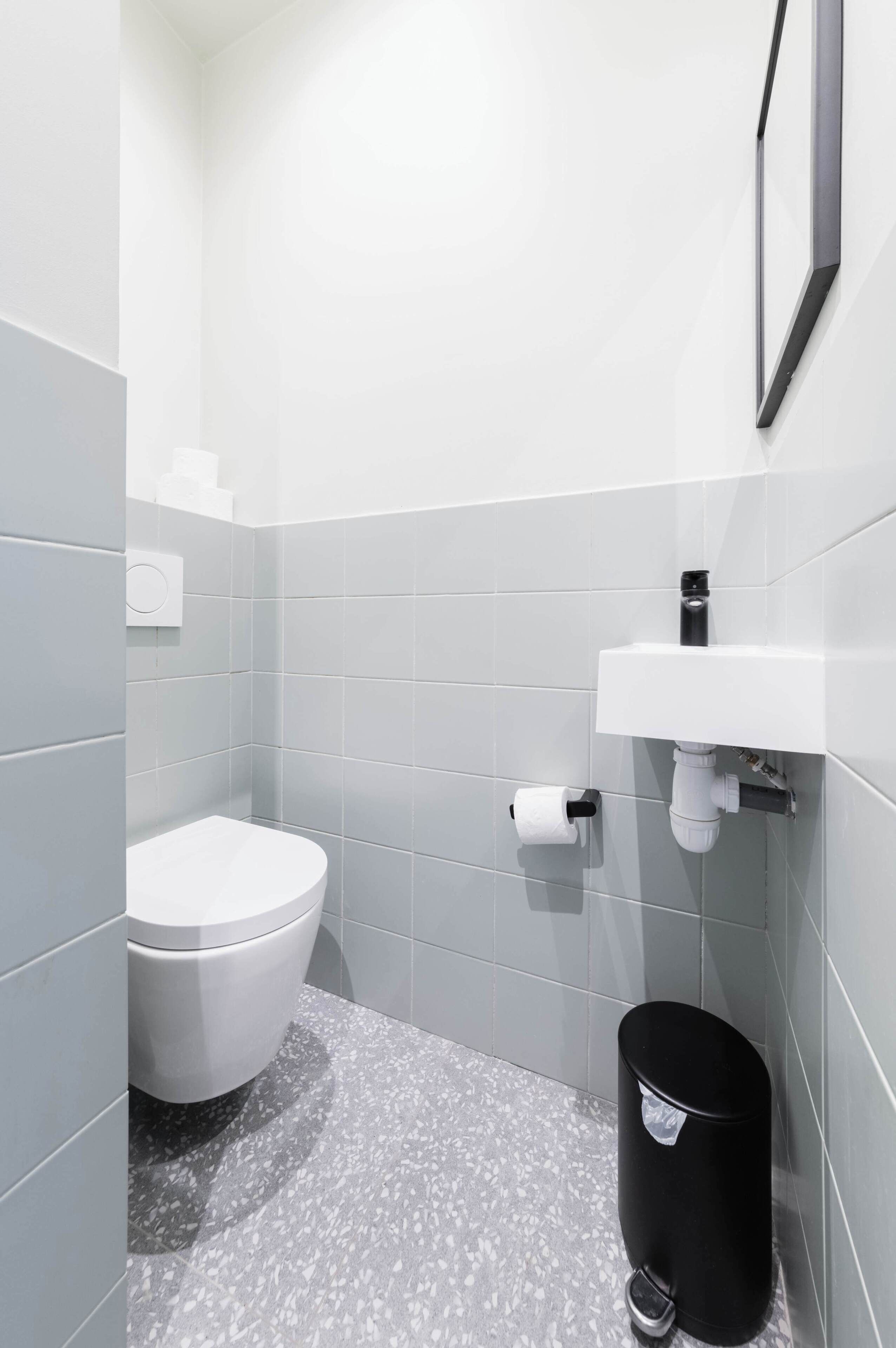A modern bathroom with a toilet, a sink, and a trash bin.