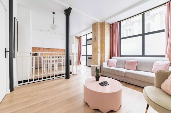 Una sala de estar moderna con un sofá, una mesa de centro redonda y vistas de la ciudad a través de grandes ventanales.