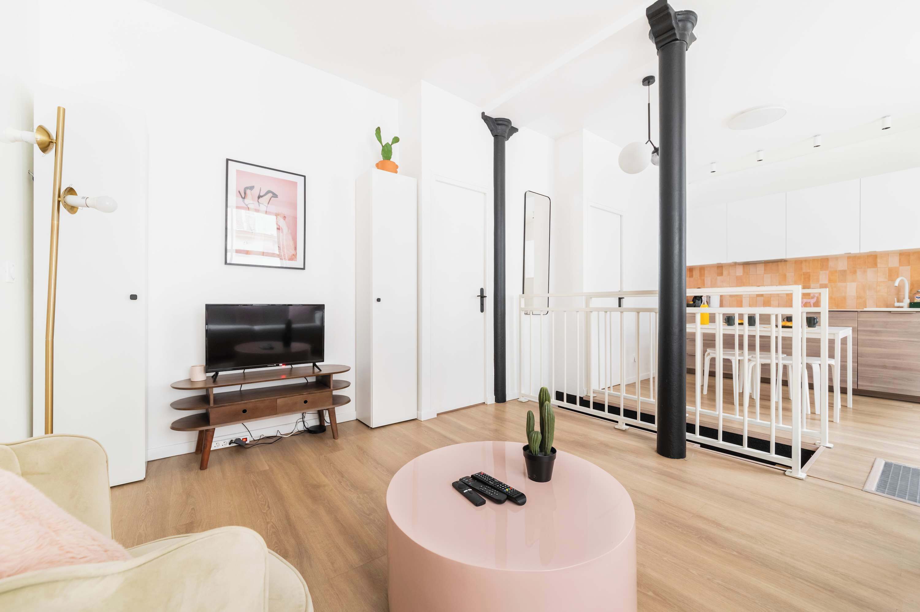 A modern living room with a flat-screen TV, a round coffee table with remote controls, a sofa, and a dining area with a white fence.