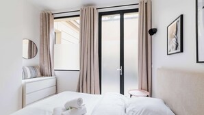 Une chambre d’hôtel avec un lit, une table de chevet, une lampe, une fenêtre avec des rideaux et un tableau encadré au mur.
