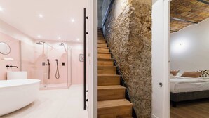 Une salle de bain moderne avec une baignoire sur pieds, un espace douche doté de plusieurs pommes de douche, et un escalier menant à une chambre à coucher avec un lit et des oreillers.