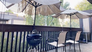 A covered patio area with a barbecue grill and outdoor furniture under large umbrellas.