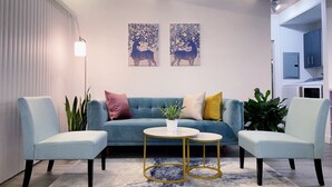 A modern living room with a blue sofa, two armchairs, a coffee table, and two wall art pieces.