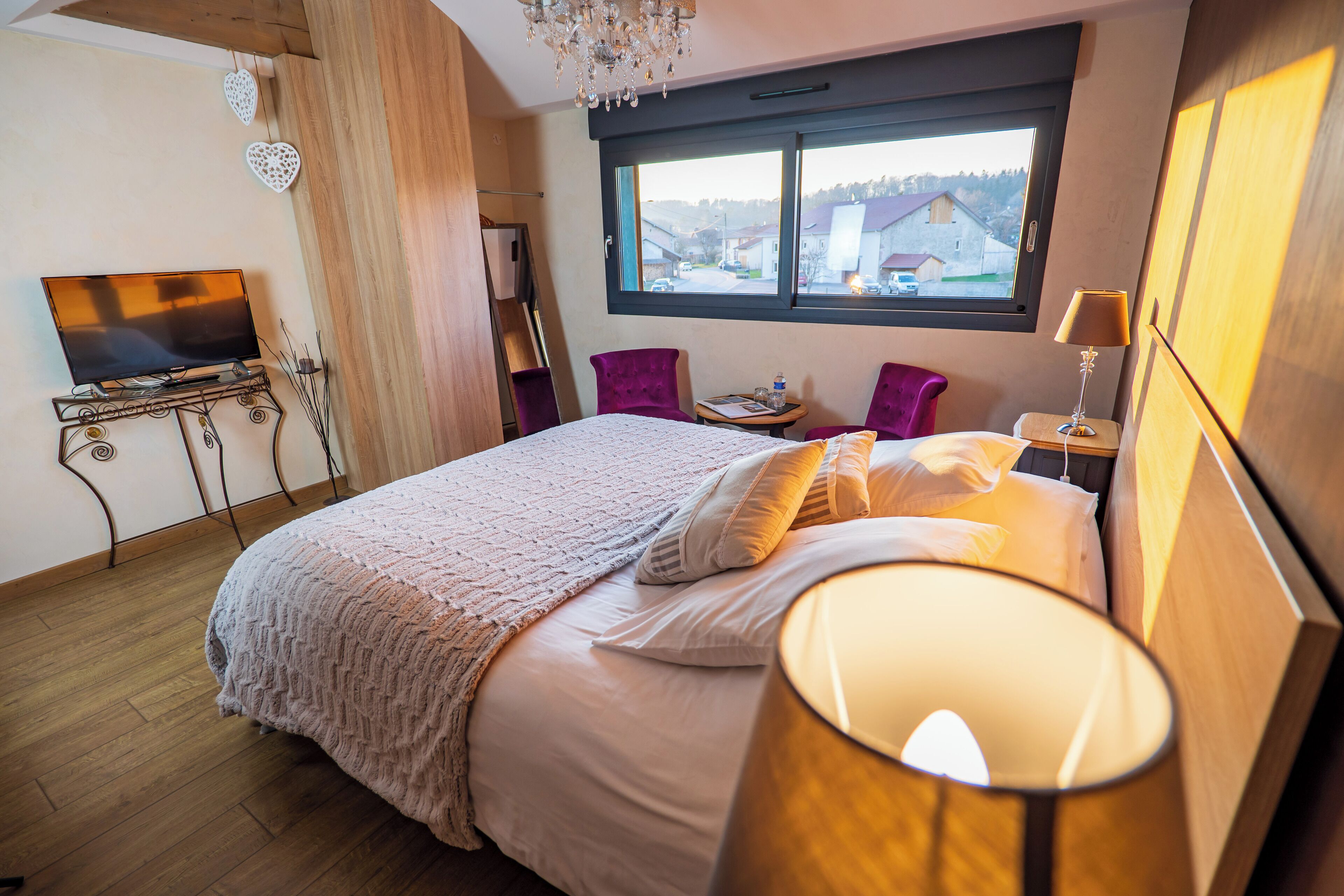 A bedroom with a bed, a TV on a side table, a window with a view, and a chandelier.