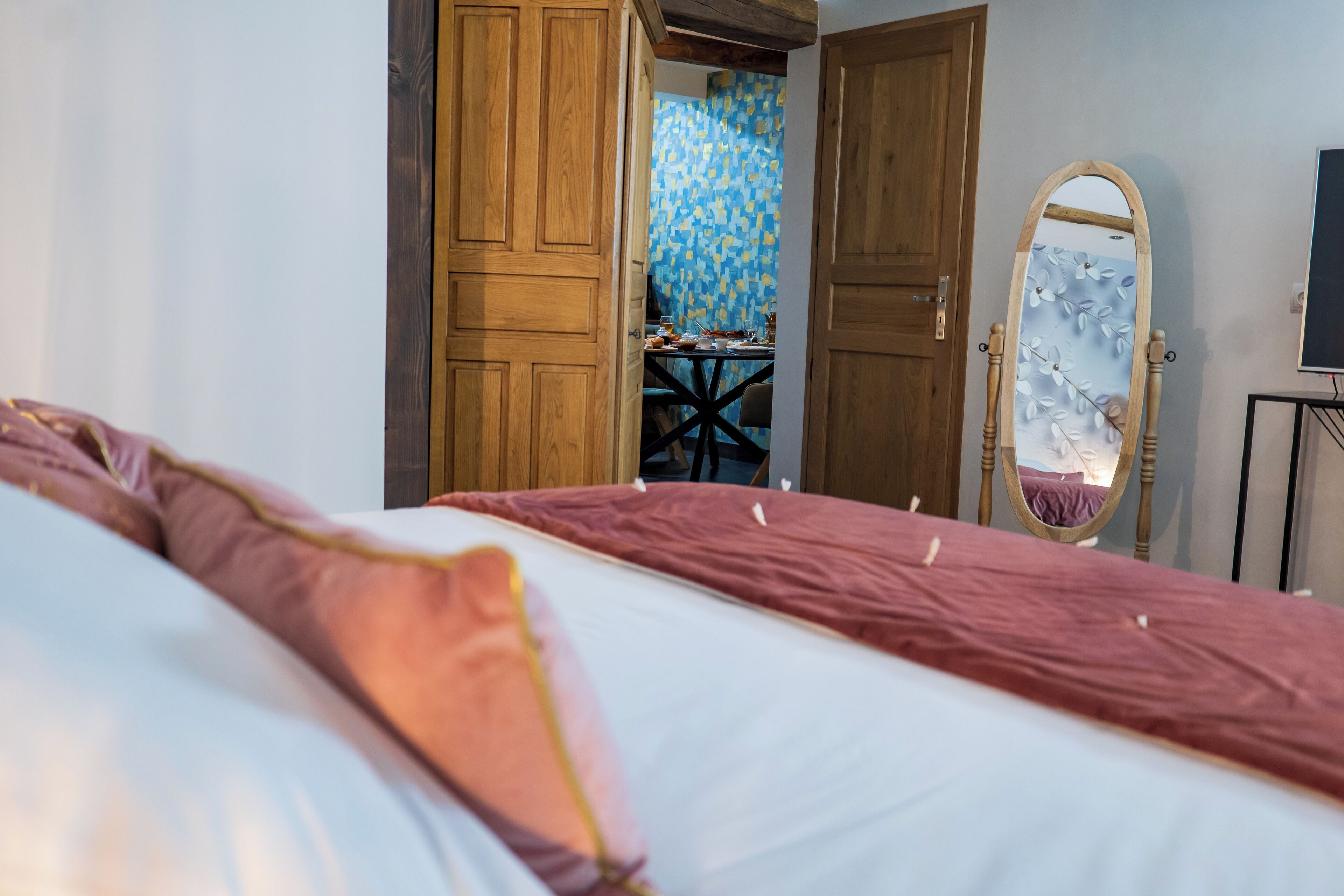 A bedroom with a bed, wooden doors, a mirror, and a small table with chairs.