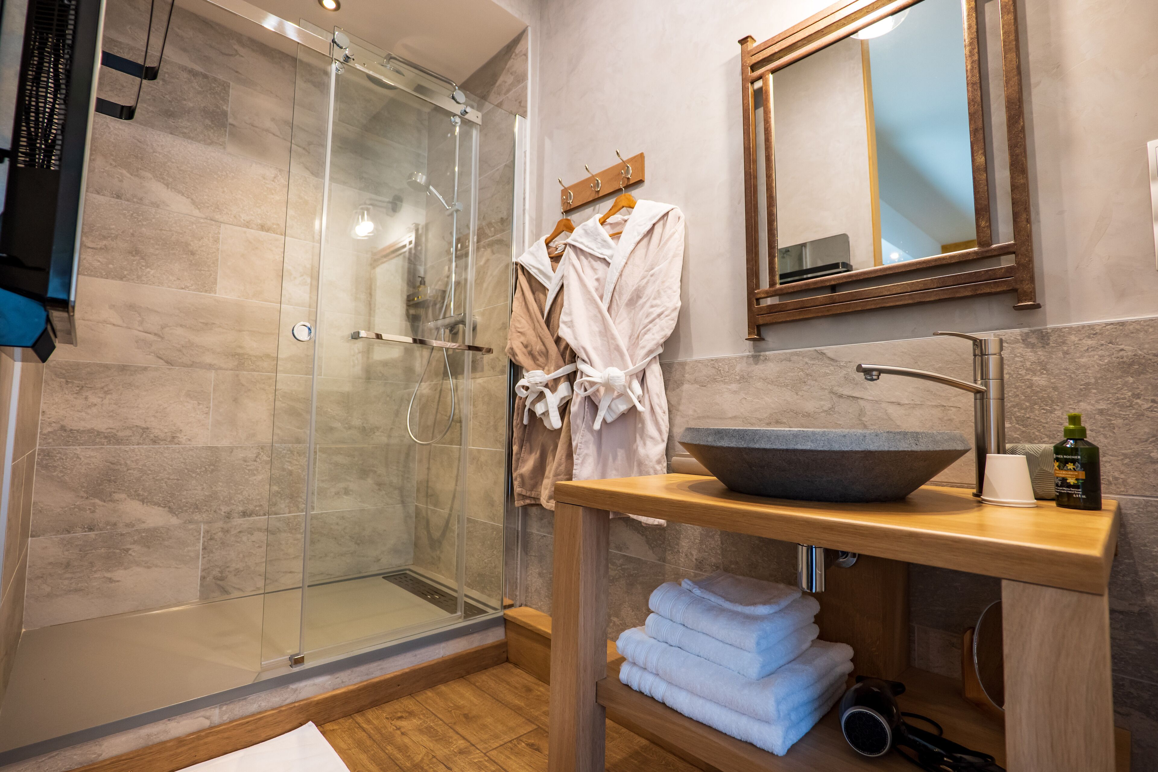 Une salle de bain moderne avec une douche à l’italienne en verre, un meuble-lavabo en bois doté d’un grand évier et un miroir au-dessus du meuble-lavabo.