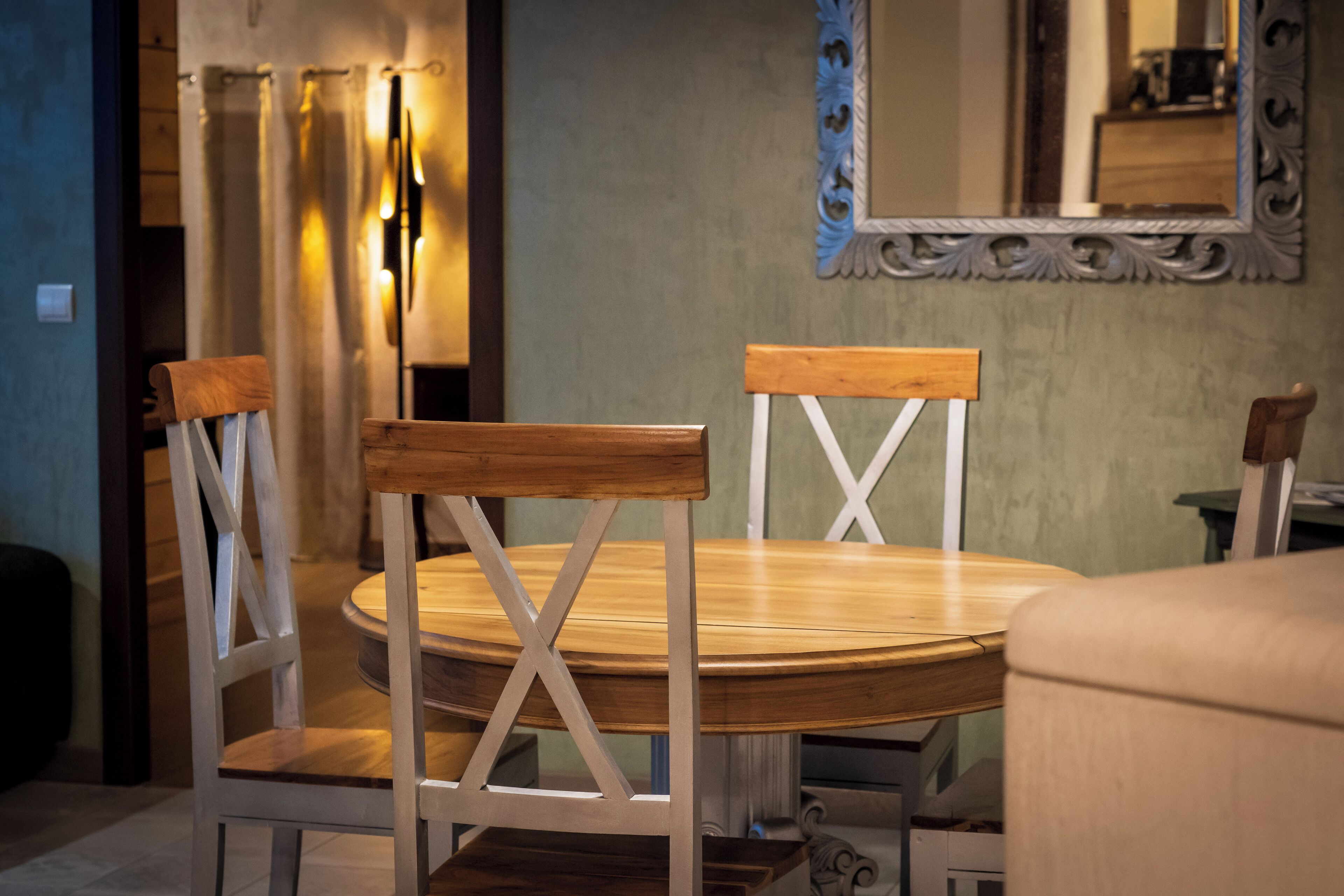 A round wooden dining table with four chairs, each with a wooden backrest and white frame.