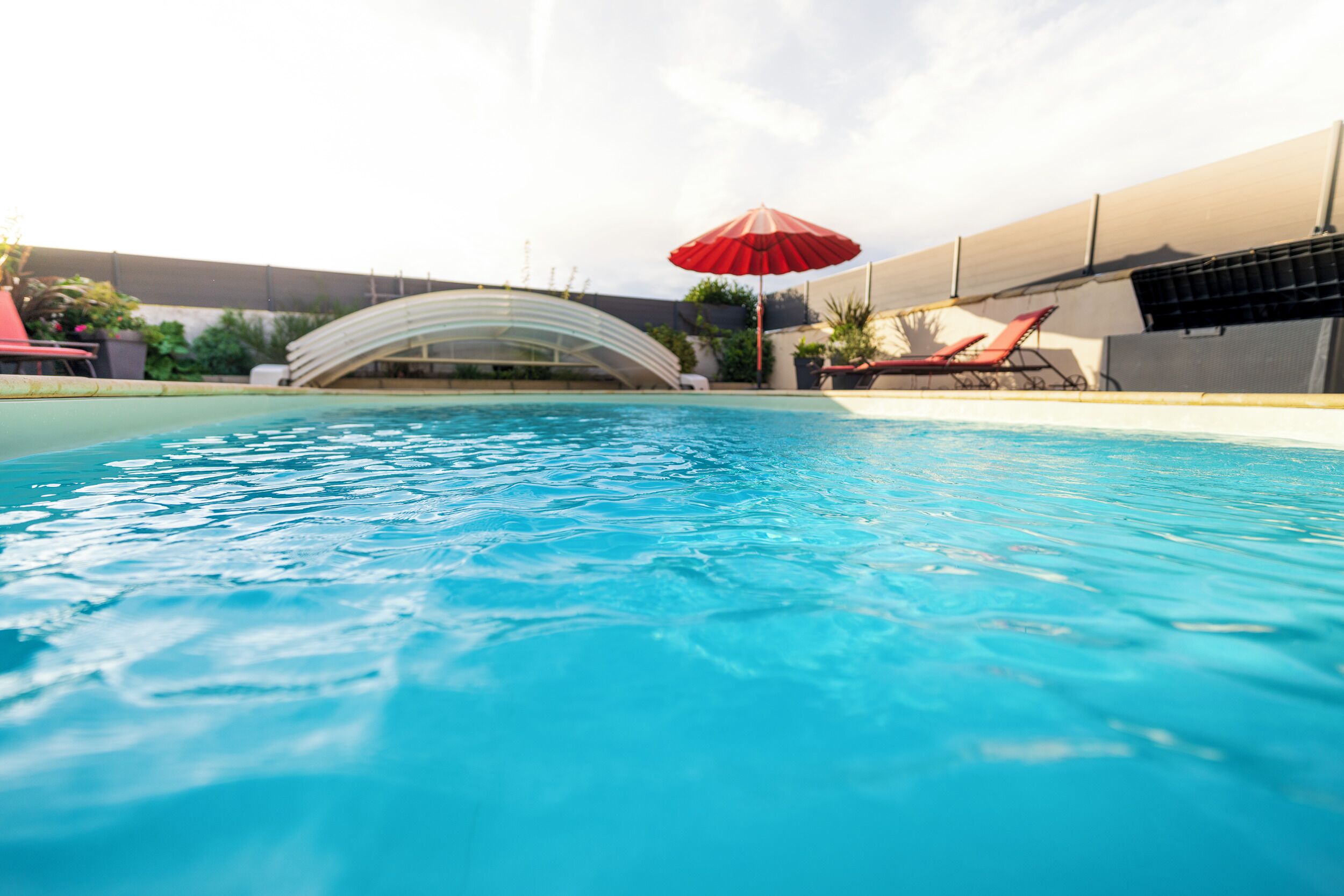 Una piscina con acqua cristallina blu, un ombrellone rosso e una struttura in vetro curvo sullo sfondo.