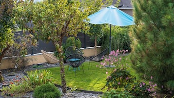 Ein Garten mit Rasen, einem Baum, einem Stuhl und einem blauen Sonnenschirm.