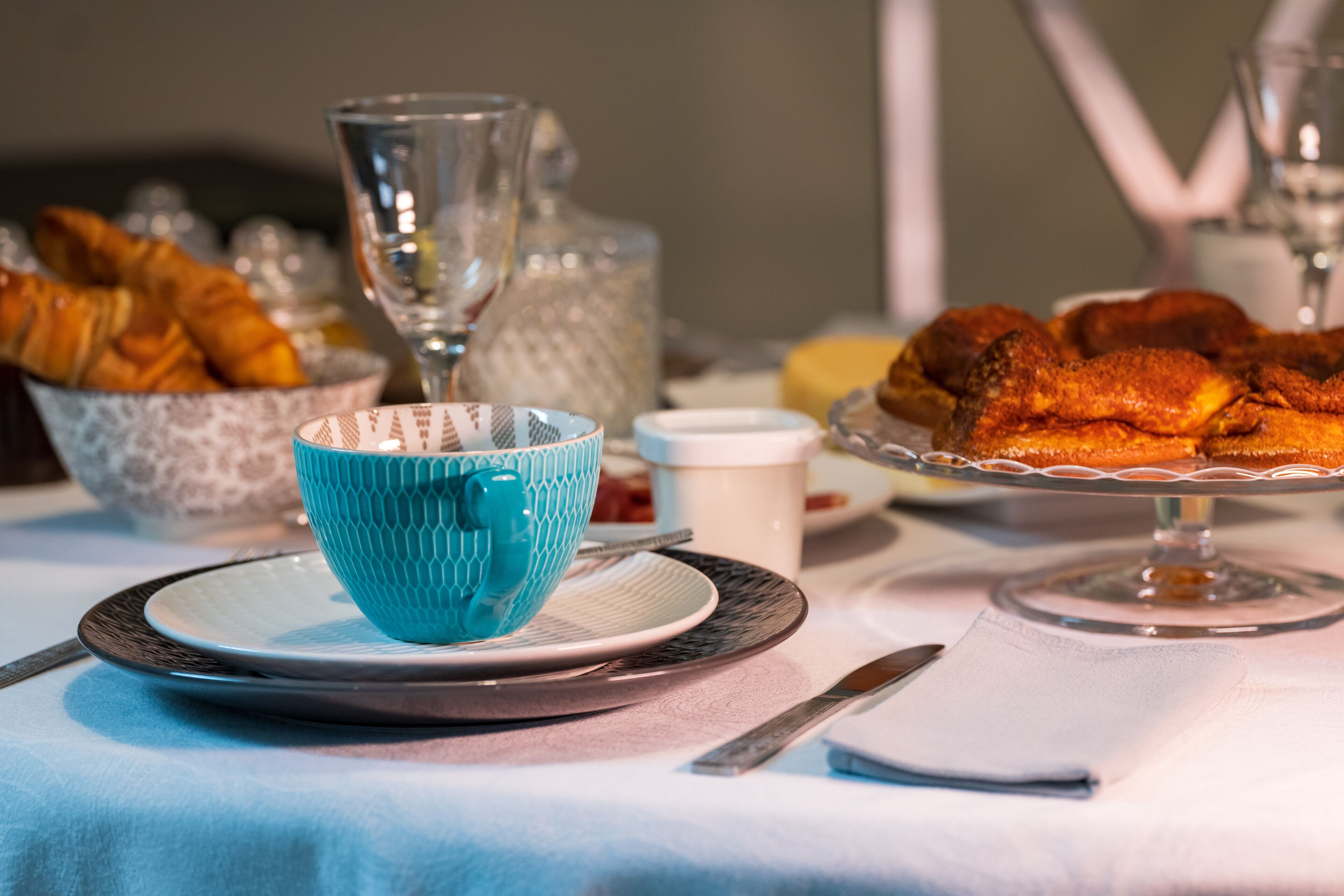 A breakfast setting with croissants, a blue cup, and a glass pitcher on a table.