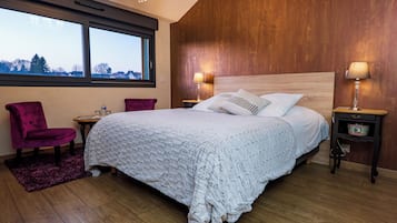 A bedroom with a large bed, wooden walls, a window, and a chandelier.