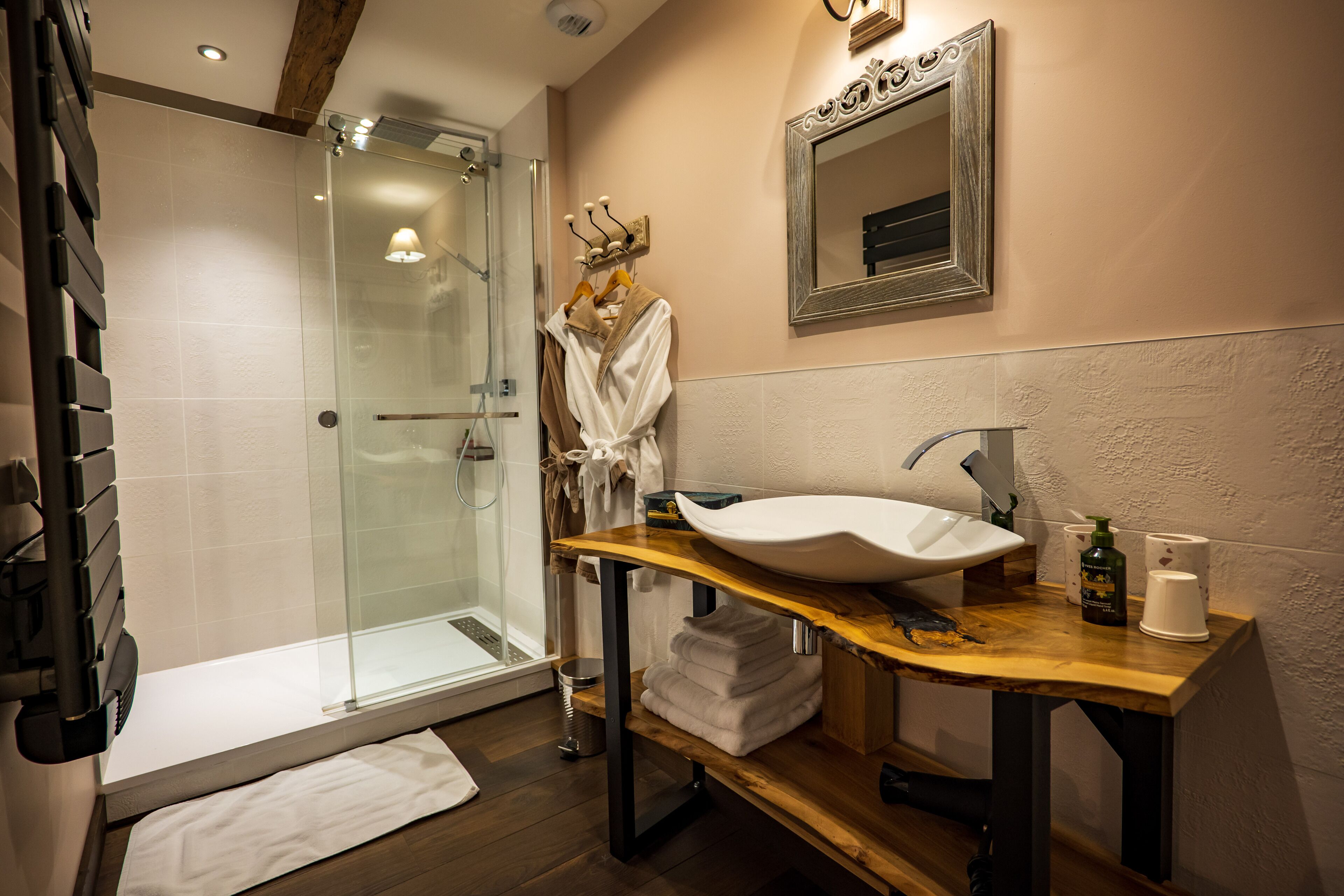 Un baño con ducha de vidrio, tocador de madera con lavamanos blanco y espejo sobre el lavamanos.
