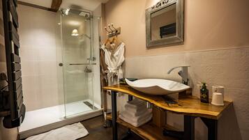 Un baño con ducha de vidrio, tocador de madera con lavamanos blanco y espejo sobre el lavamanos.