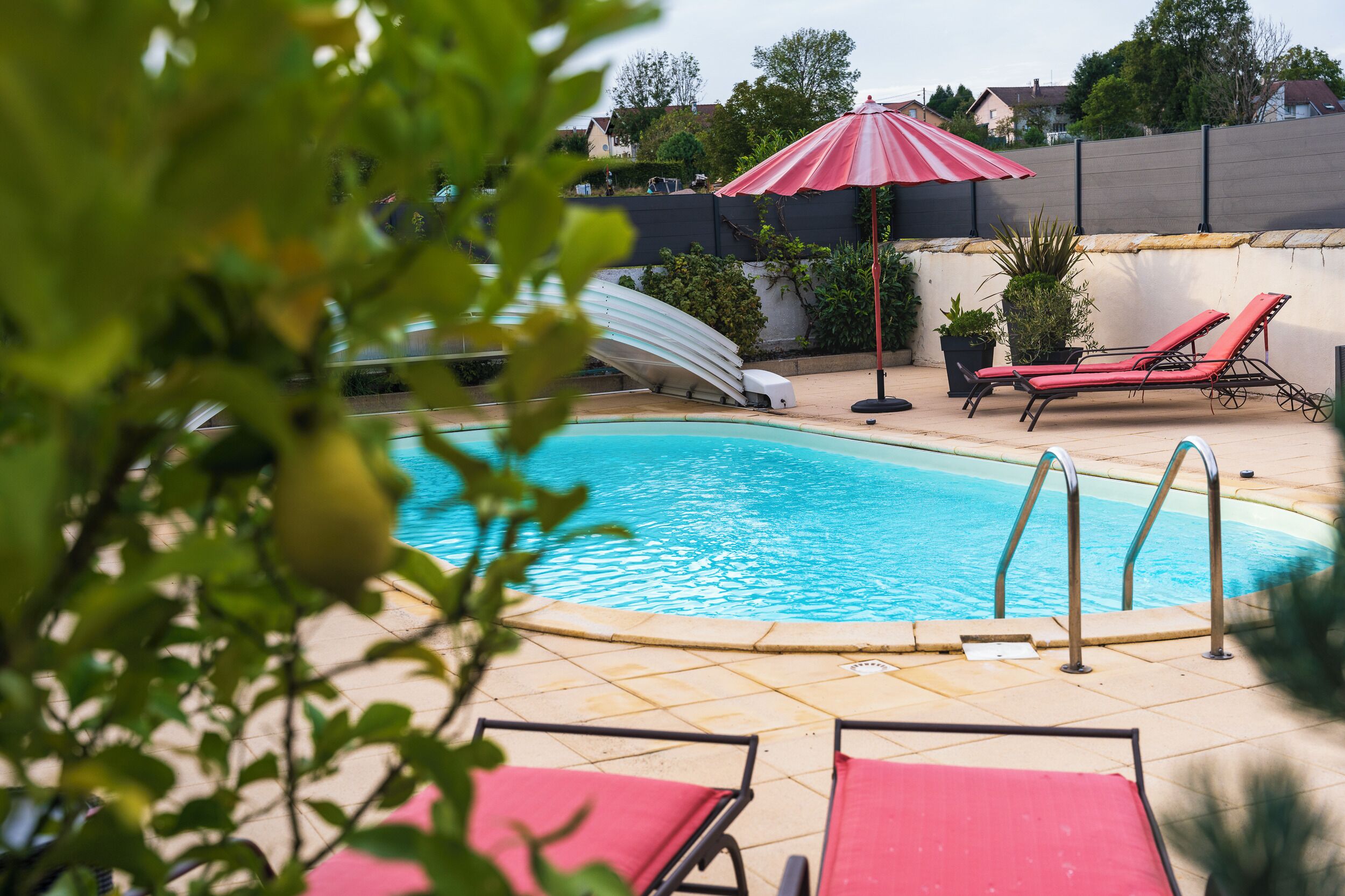 Une piscine dotée de chaises longues et d’un toboggan, entourée d’une clôture et agrémentée de plantes en pot.