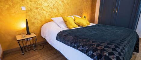 A bedroom with a bed, wooden floor, a nightstand with a lamp, and a wardrobe.