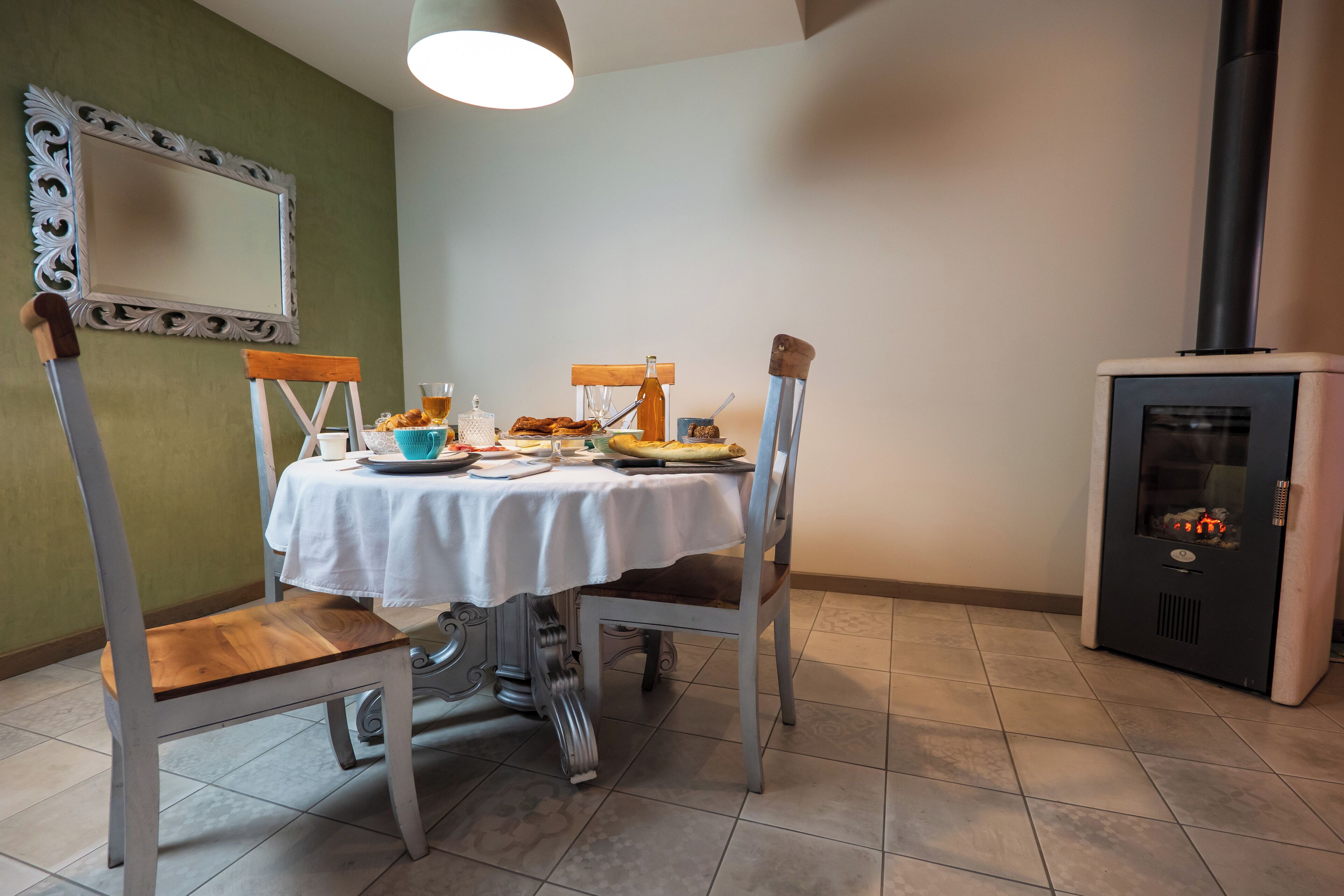 A dining area with a table set for two, chairs, a small table with a bottle and glasses, and a wood-burning stove.
