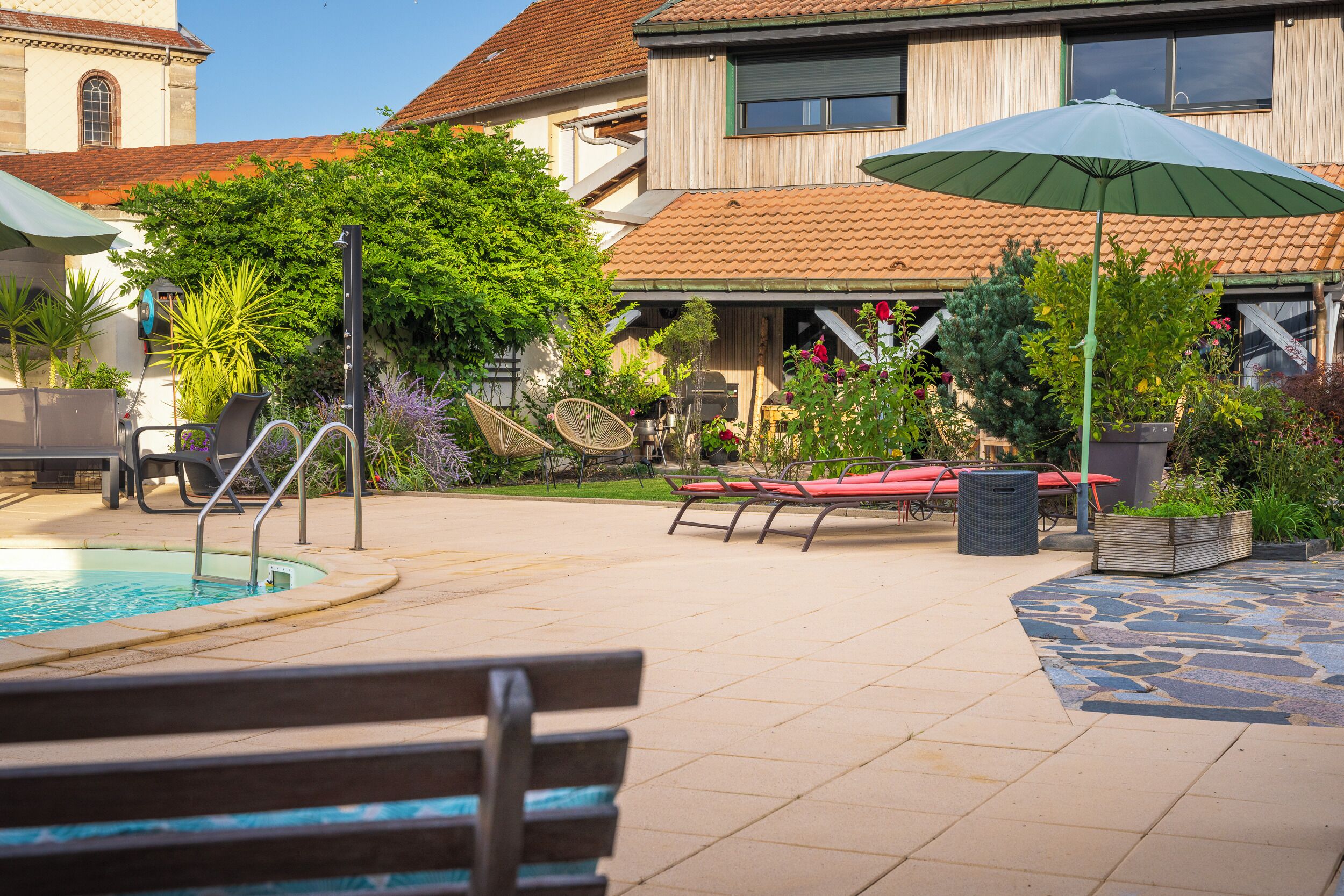 A pool area with a bench, lounge chairs, and a covered seating area.