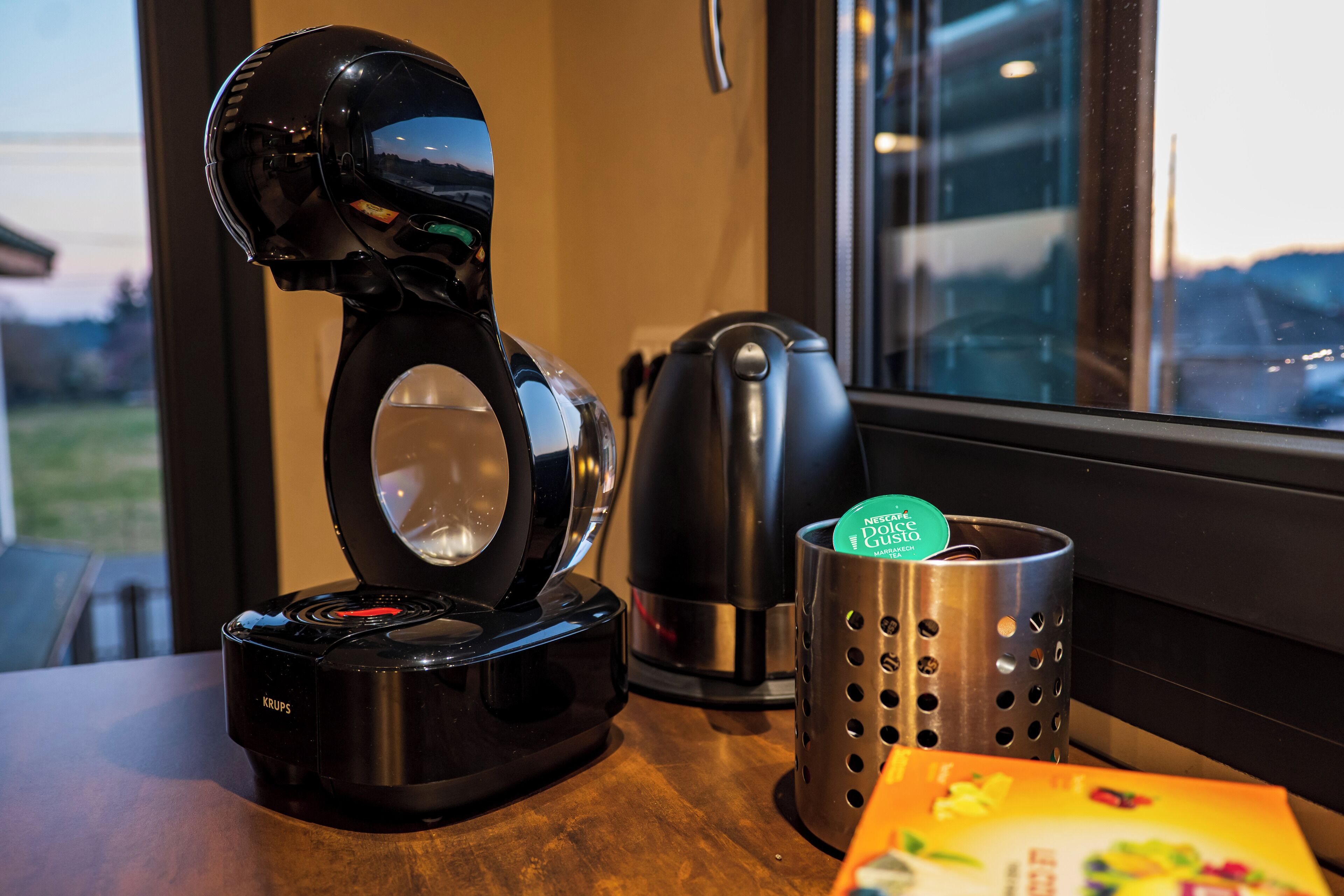A coffee maker, a kettle, and a mug on a wooden table.