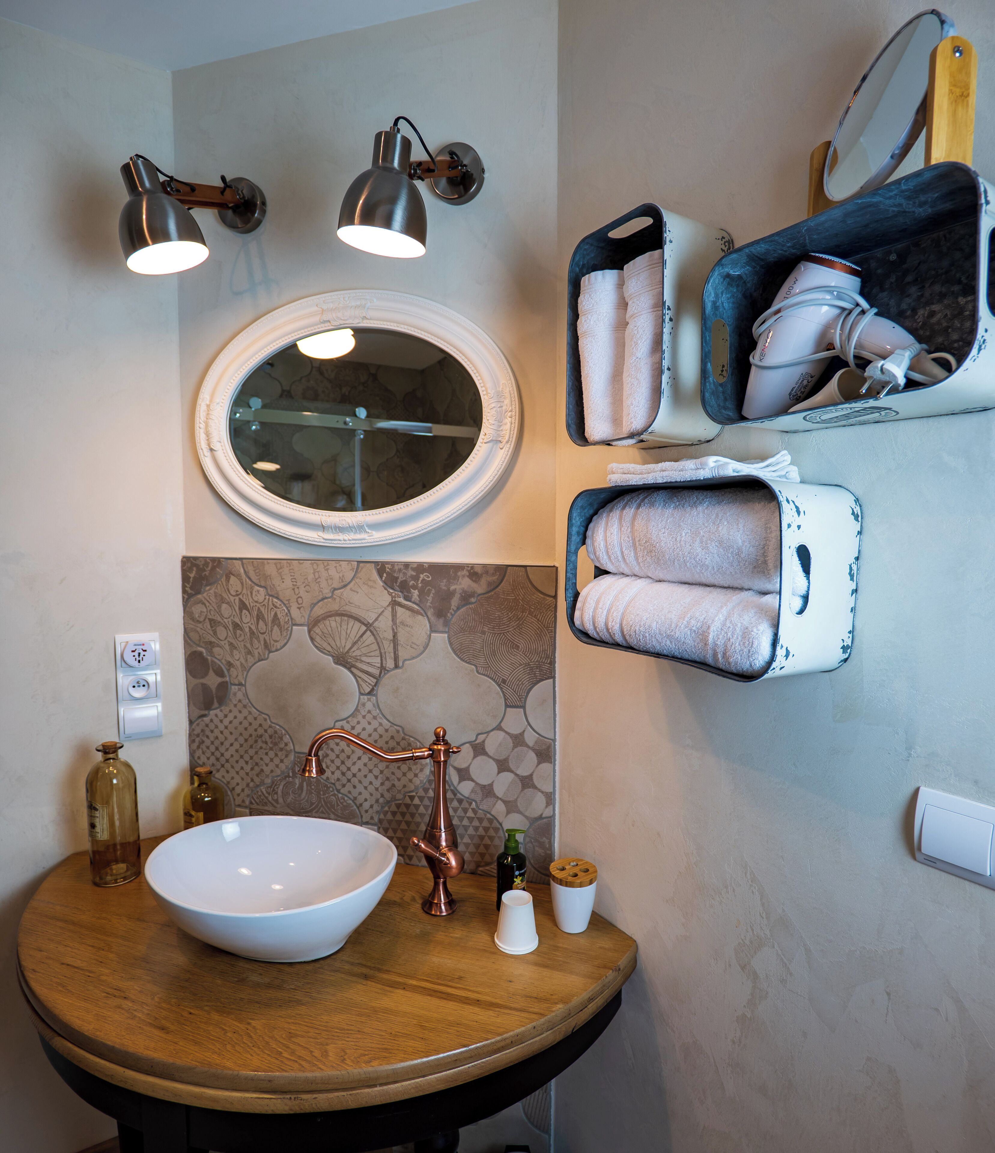 A bathroom with a round wooden sink, a copper faucet, a large mirror, and two wall-mounted lamps.