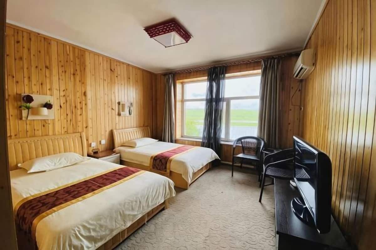 A room with two beds, a desk, a chair, and a window with a view of the outdoors.