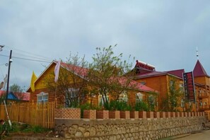 A wooden house with a stone wall foundation, a red roof, and a small garden area. - Erguna, room, Wertley, Domiega resort (Ergun)