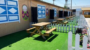 A row of wooden picnic tables and benches, a white picket fence, and a building with colorful murals.