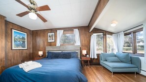 Un dormitorio con una cama grande, ventilador de techo, sofá y ventana con cortinas.