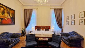 A hotel room with a large bed, two armchairs, a chandelier, a painting, and framed pictures on the wall. - Palais Kneissl (Burgau)