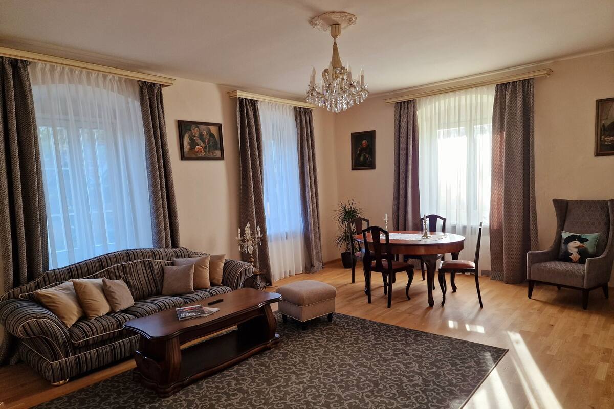A living room with a sofa, coffee table, dining table, chairs, and a chandelier.