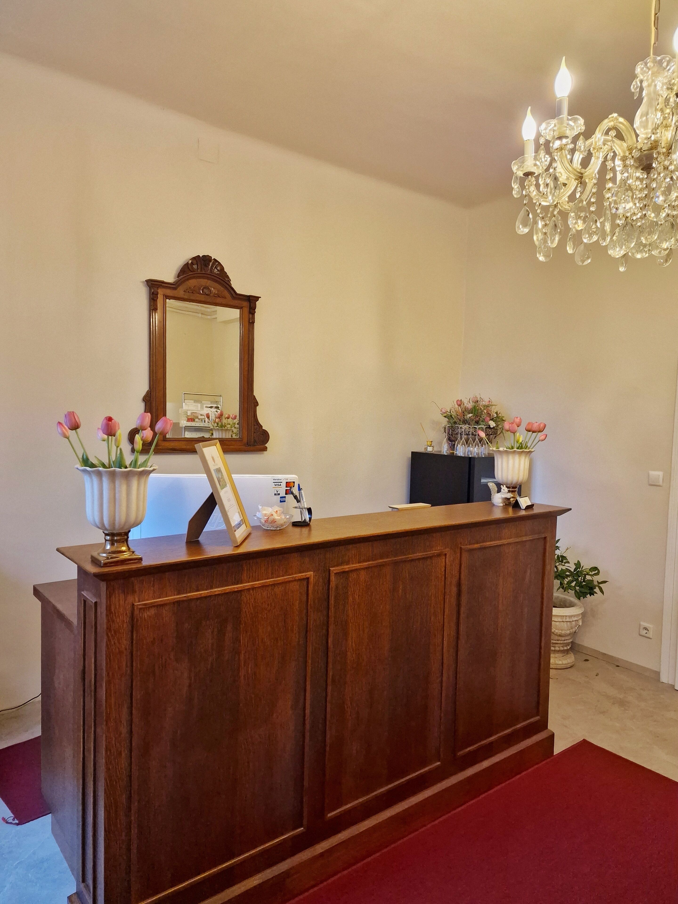 A reception desk with a mirror, a vase with flowers, and a chandelier.