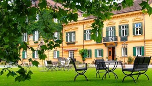 A yellow building with green shutters, a balcony, and outdoor seating. - Palais Kneissl (Burgau)