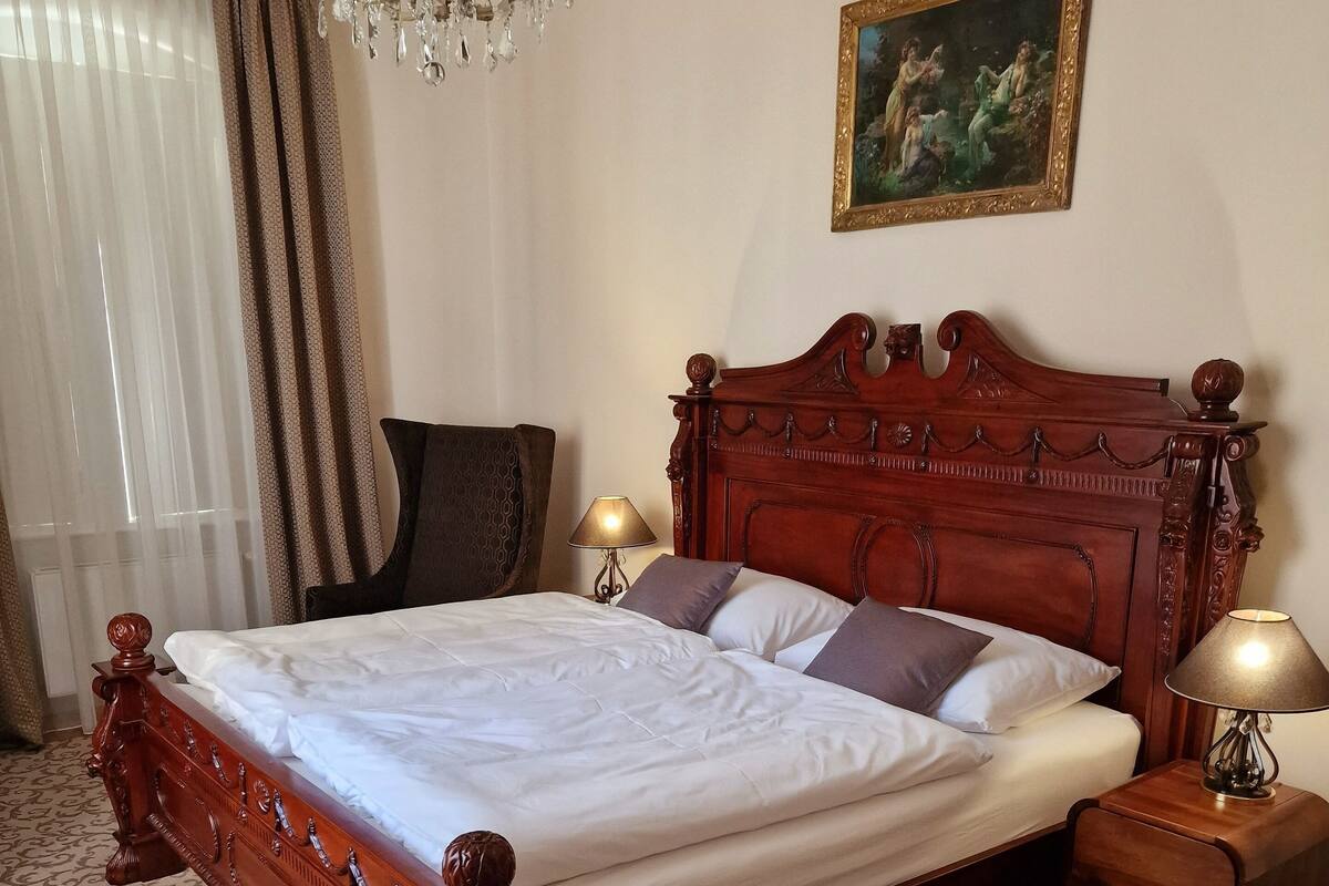 A bedroom with a wooden bed, a chandelier, a painting, and a patterned rug.