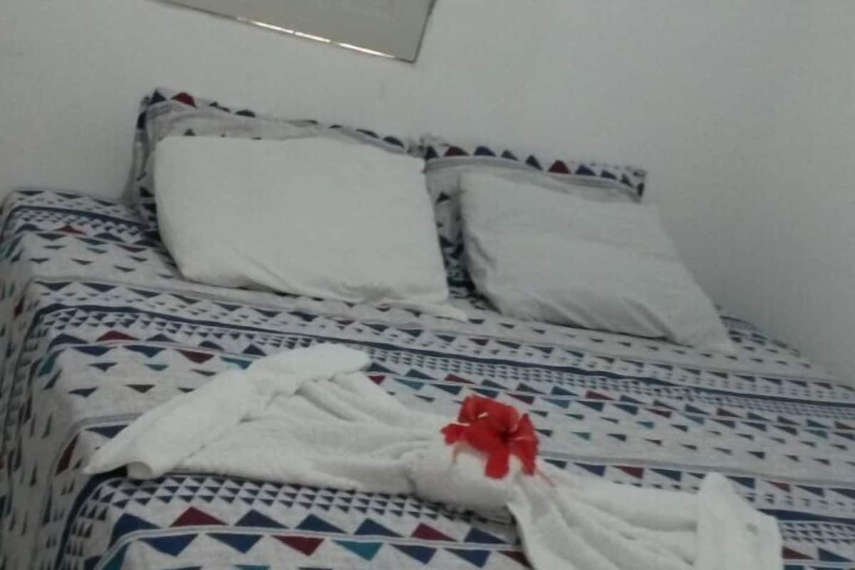 Una cama con ropa de cama estampada, un almohón blanco y un lazo rojo.