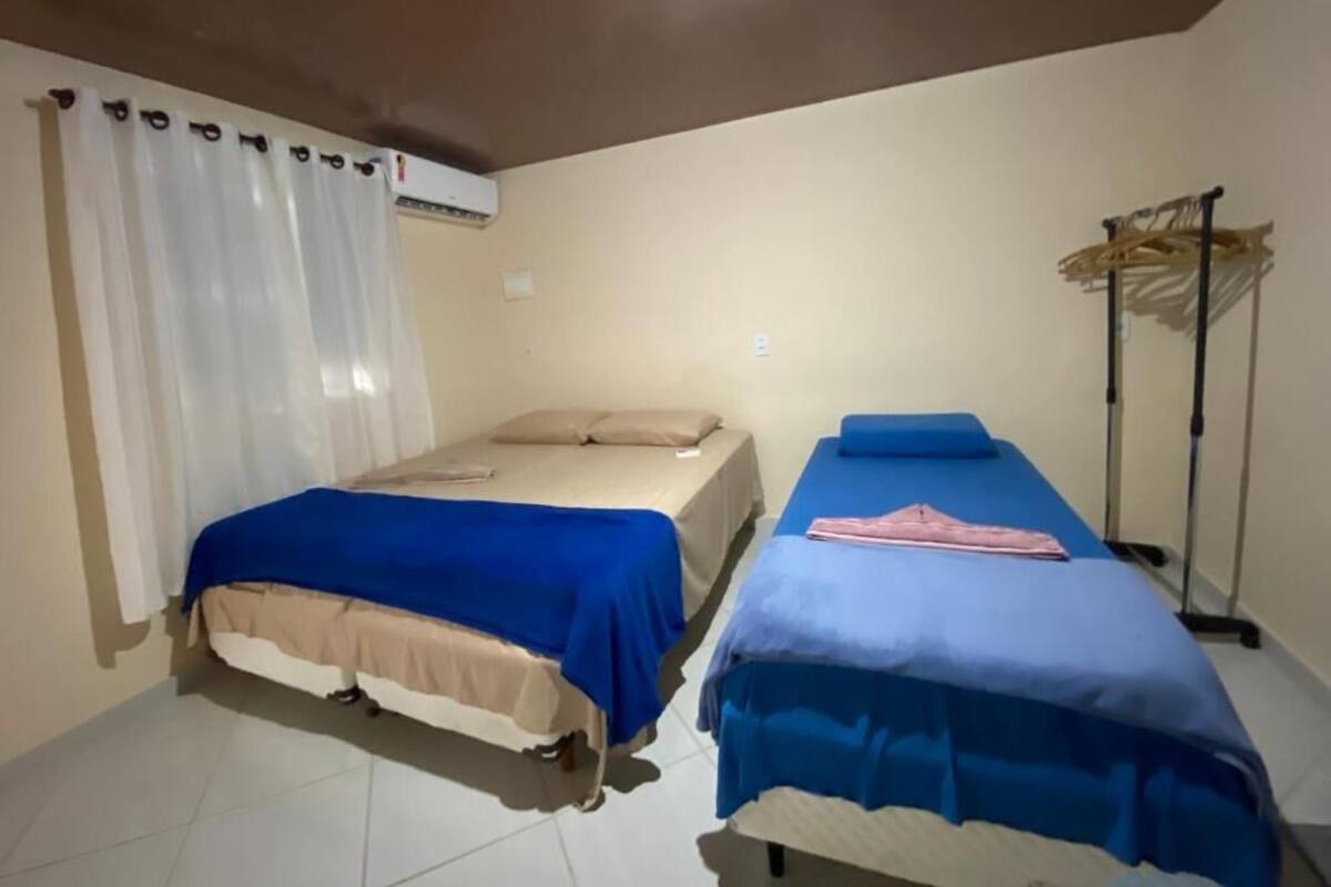 Dos camas individuales con ropa de cama azul y beige, un ventilador de techo y un calefactor.