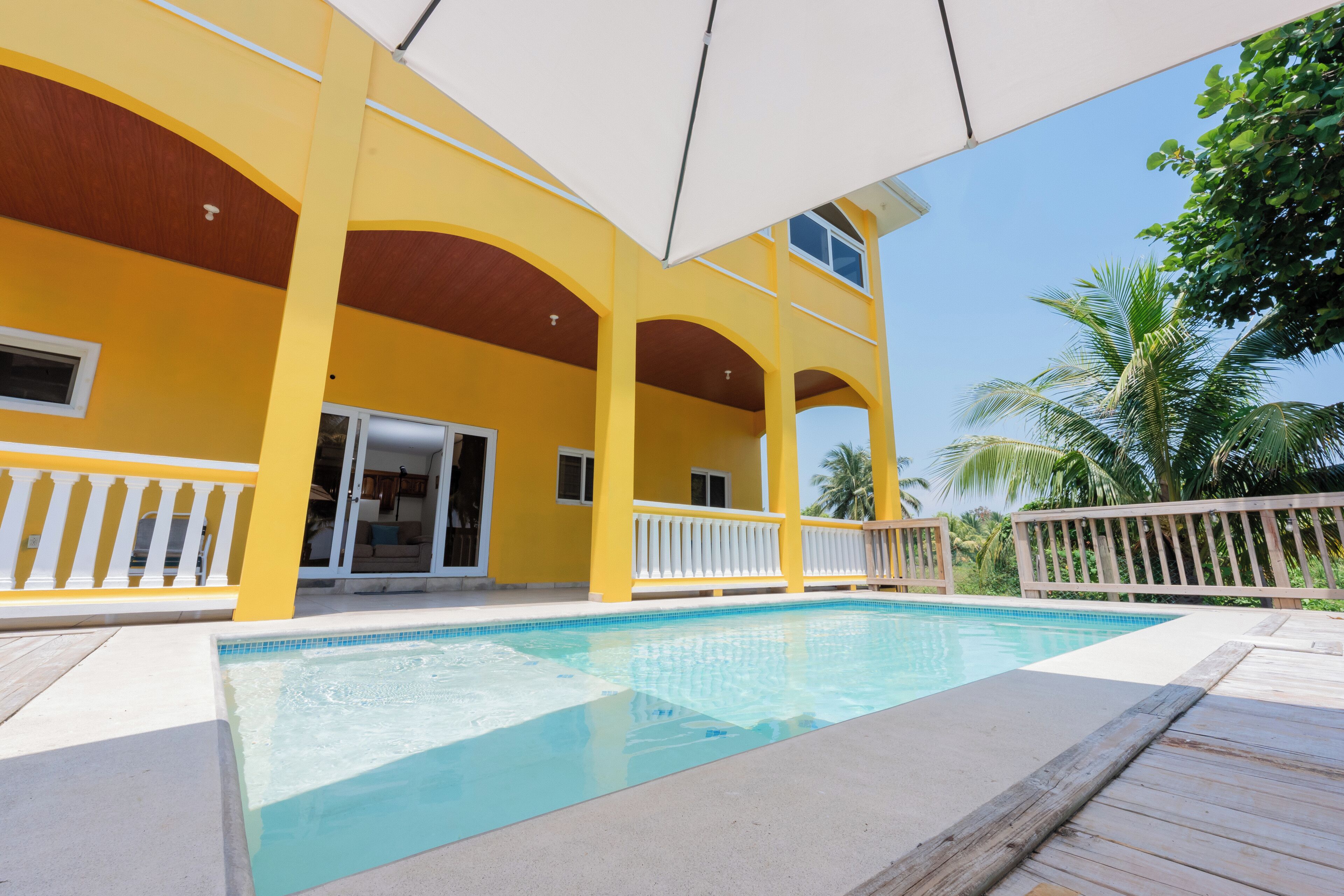 A pool area with a yellow building, white railings, and palm trees.