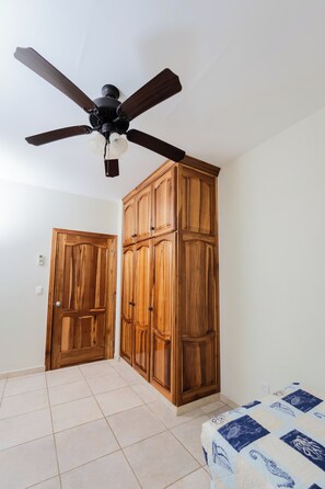 A room with a ceiling fan, wooden wardrobe, a door, and a bed with a patterned bedspread. - Frente al mar con piscina! En Tela (Tela)
