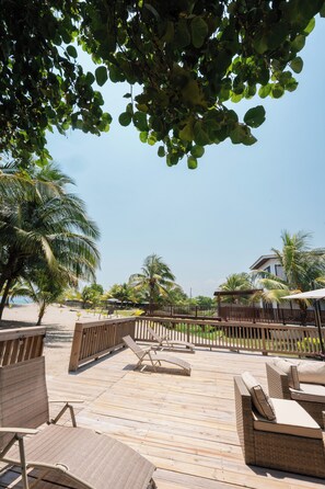 A wooden deck with lounge chairs and a wooden fence, surrounded by palm trees and a clear sky. - Frente al mar con piscina! En Tela (Tela)