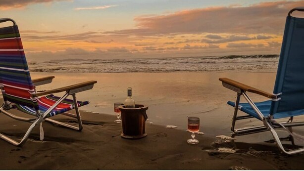 Dos sillas de playa mirando al océano con un atardecer de fondo.