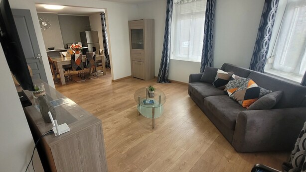 Ett modernt vardagsrum med en grå soffa, ett soffbord i glas och en matplats med ett bord och stolar i trä.