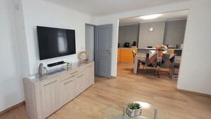 Ett modernt vardagsrum med en platt-TV, ett träskåp och en matplats med orange skåp och ett bord.